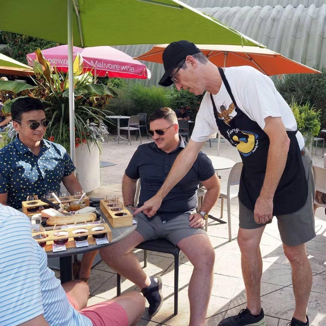 Mark Gibson in a Cheese Tango apron talking through a wine flight tasting with guests at the Malivoire patio