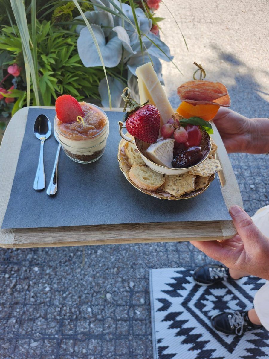 A teacup filled with cheese, strawberries and charcuterie held on a tray outdoors at the vineyard