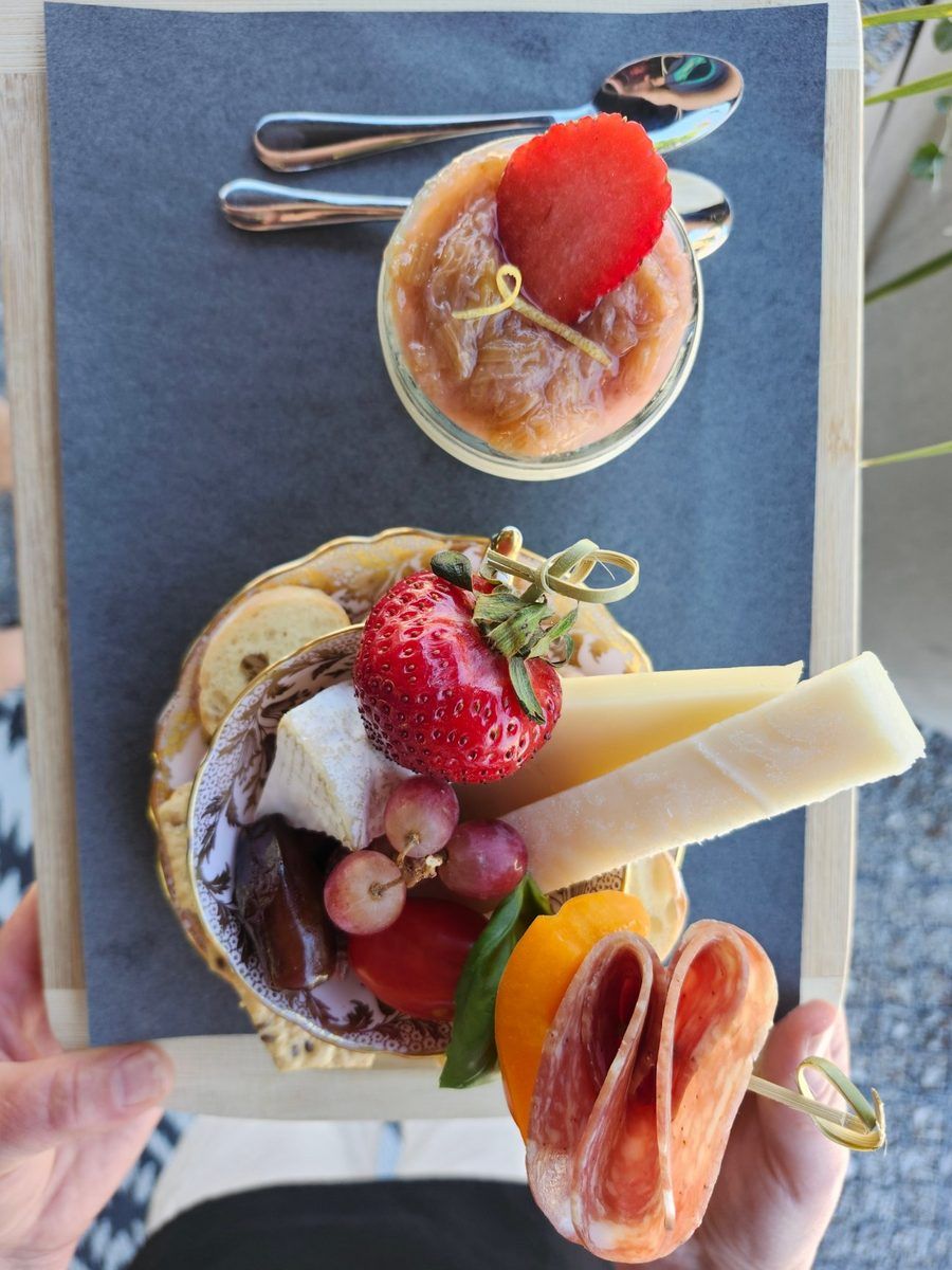 Top-down view of a teacup filled with cheese, strawberries, grapes and charcuterie, beside a dessert jar