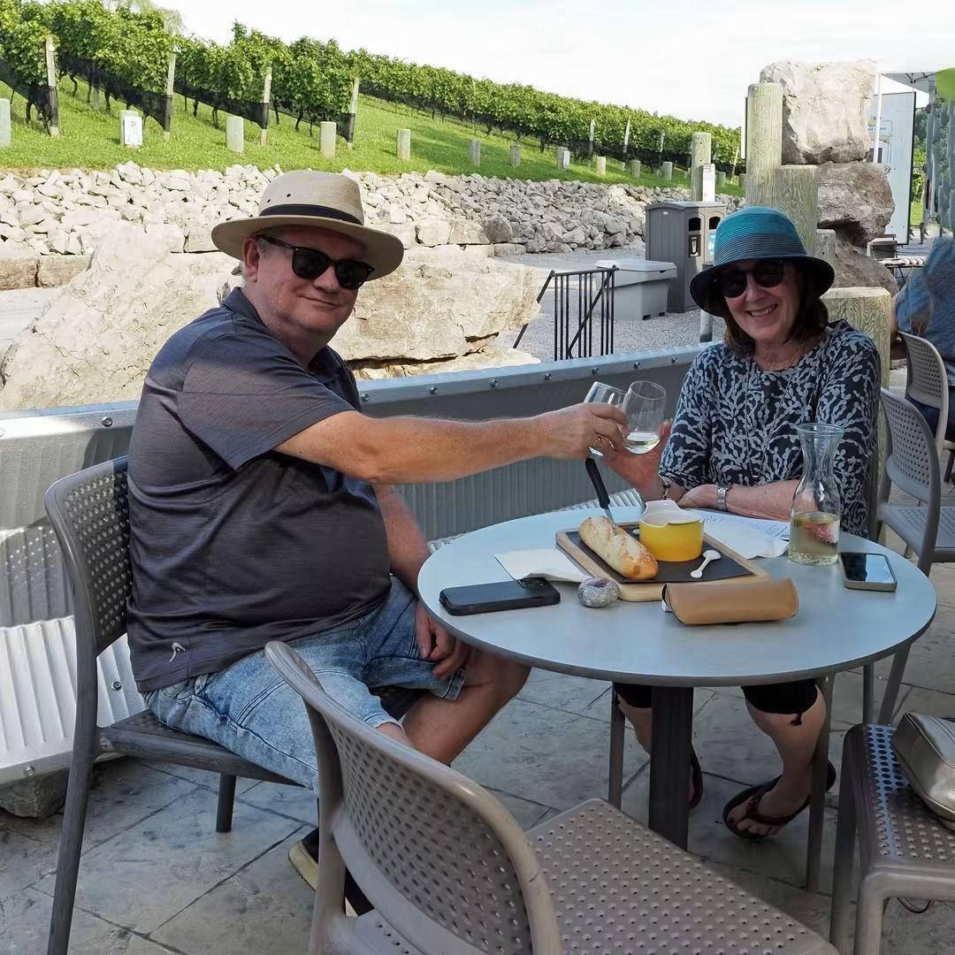 Two guests toasting with white wine at a patio table with tasting trays and cheese boards