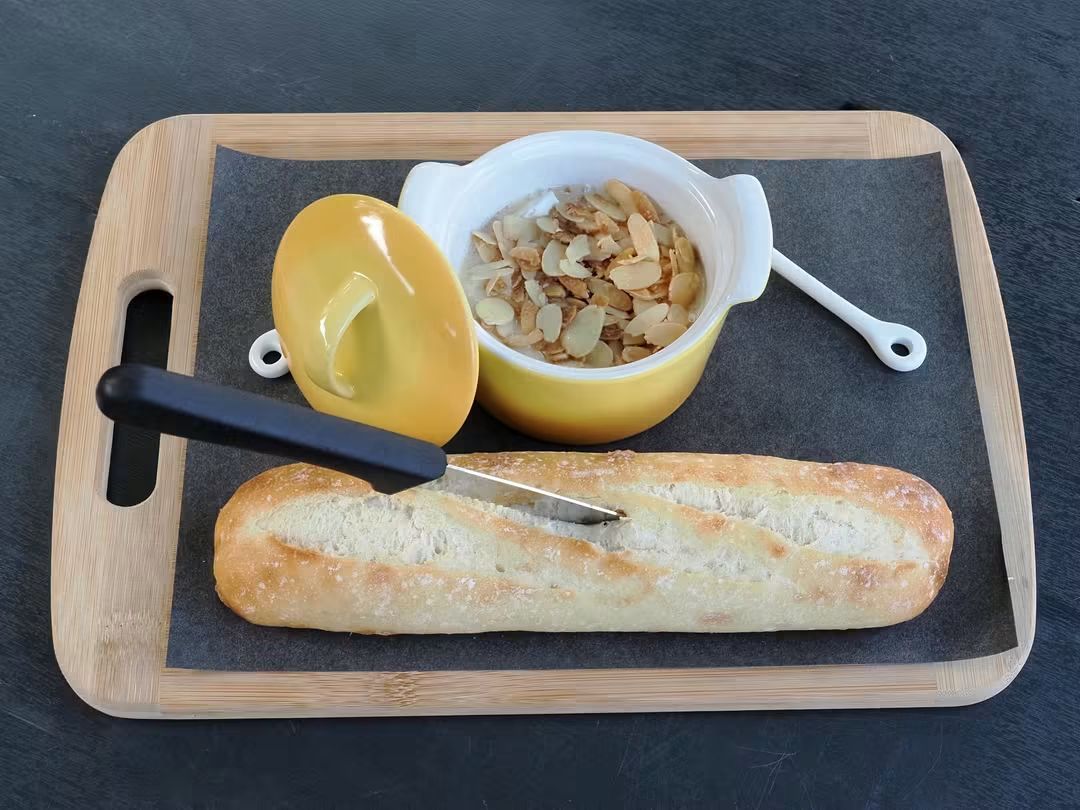 A baked cheese dip topped with toasted almonds in a yellow ramekin with a fresh baguette