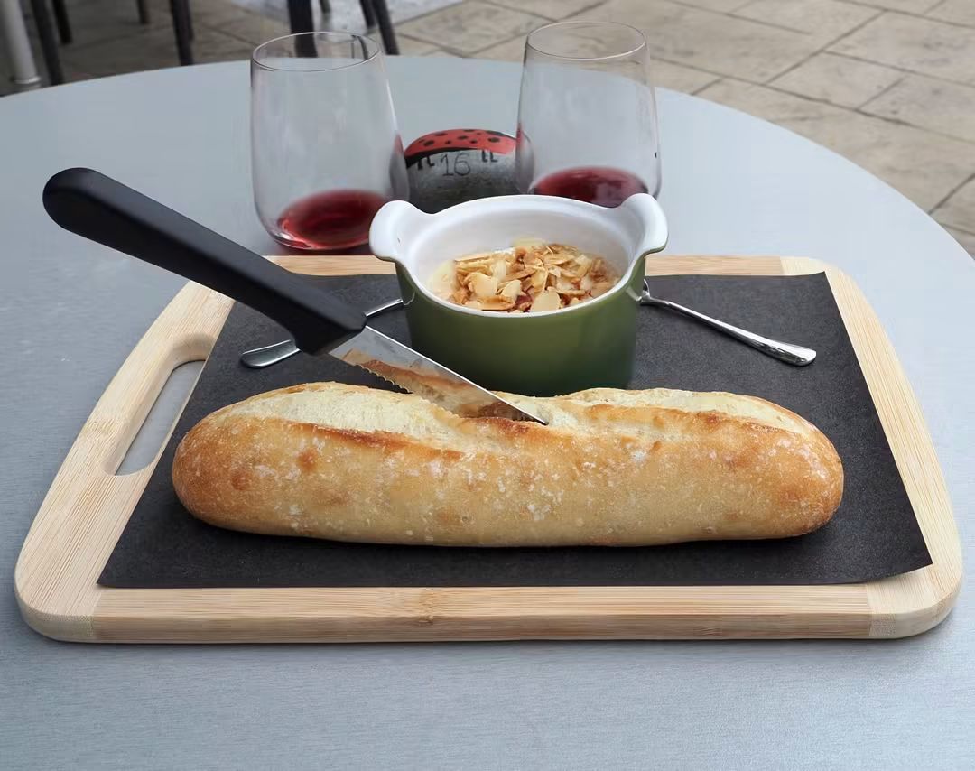 A warm dip in a green bowl with a baguette and two glasses of red wine on a patio table