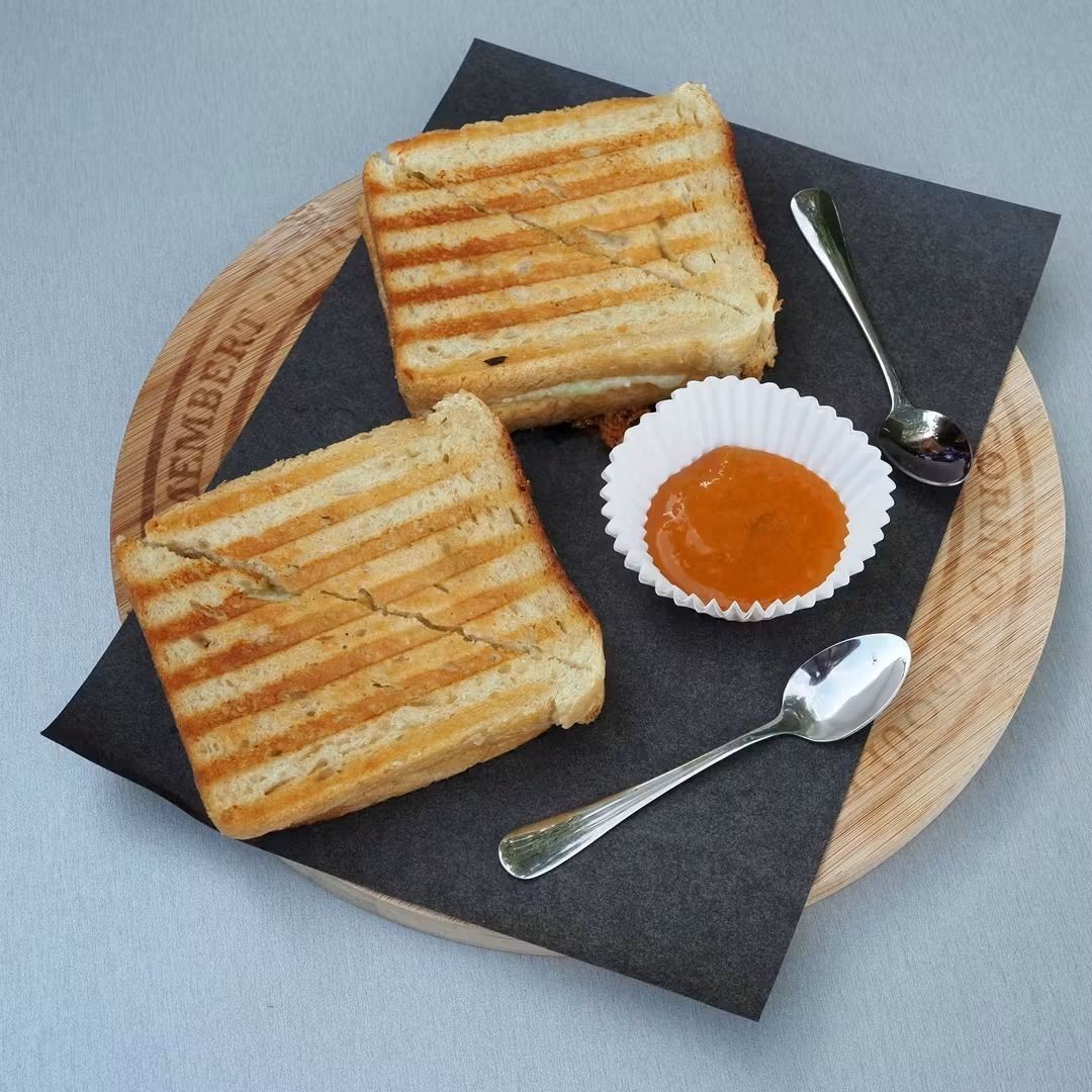 Two griddled panini halves of The BEST Grilled Cheese served with a side cup of Aprihot compote